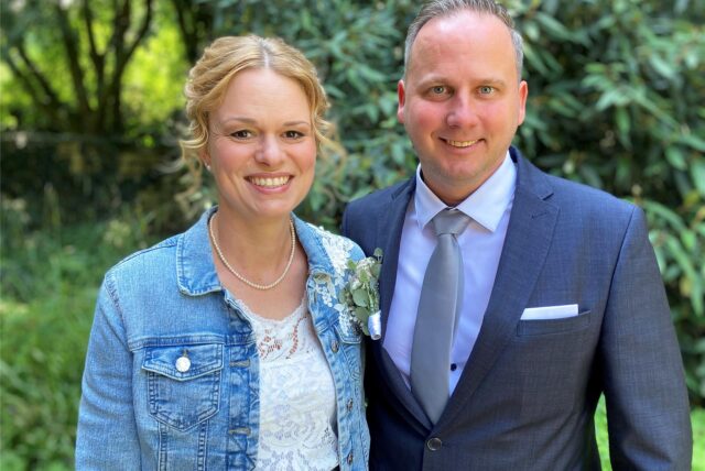Lena und Tim Wolter stehen nach ihrer standesamtlichen Trauung dicht nebeneinander und lächeln freundlich in die Kamera.