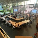 Menschen stehen und sitzen auf der Wahlparty im Bergkamener Rathaus und schauen auf Bildschirmen auf die Ergebnisse.