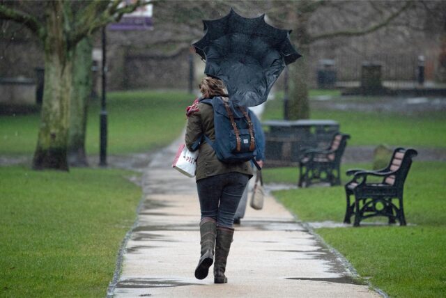 Eine Windböe drückt den Regenschirm einer Frau nach hinten.