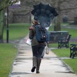 Eine Windböe drückt den Regenschirm einer Frau nach hinten.