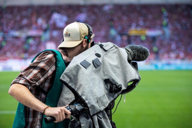 Ein Kameramann filmt vor einem Fußballspiel.