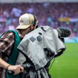 Ein Kameramann filmt vor einem Fußballspiel.