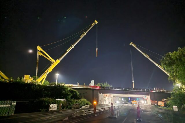 Eine A1-Autobahnbrücke bei Nacht. Links und rechts steht jeweils ein Kran. Die Baustelle ist beleuchtet.
