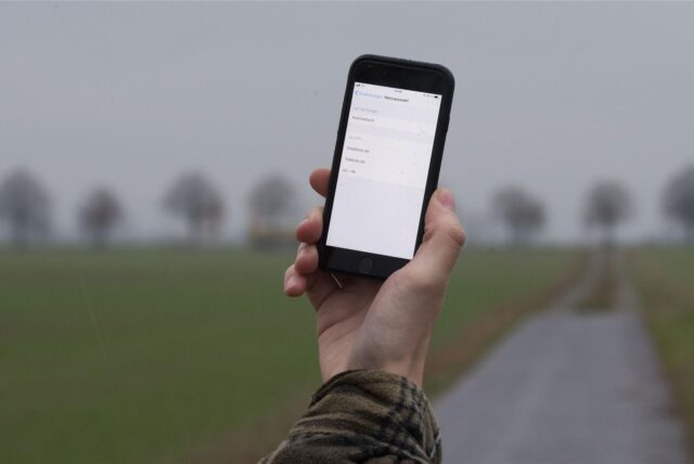 Ein Mann lässt auf einem Feldweg sein Smartphone nach Netzbetreibern suchen.