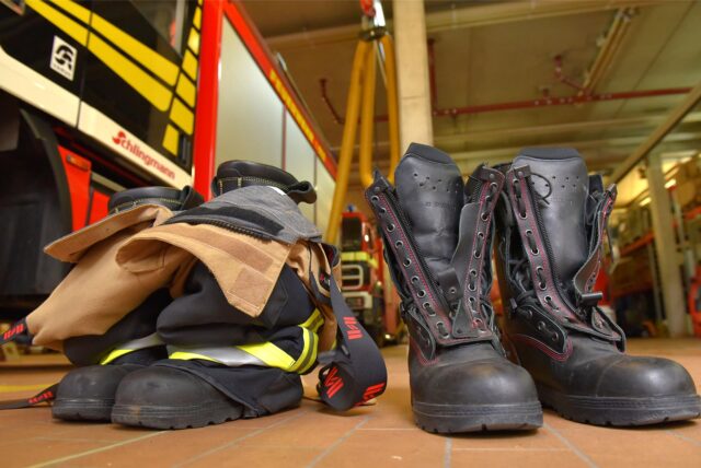 Stiefel stehen in der Feuerwache. Links sind Feuerwehrfahrzeuge zu sehen.