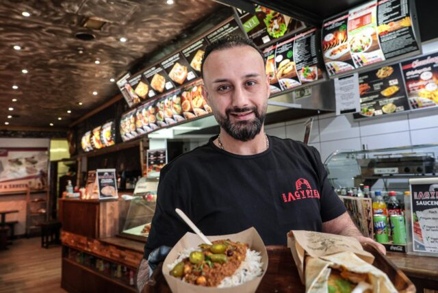 Mohsen Rabi in seinem Laden, in den Händen hält er zwei der angeboteten Gerichte.