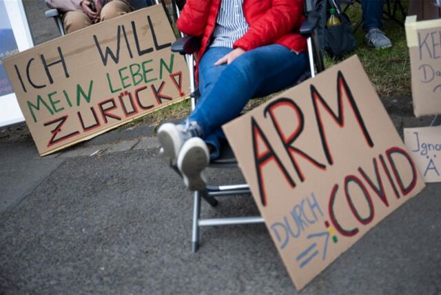 Demonstrierende von Long-Covid-Selbsthilfegruppen aus Rheinland-Pfalz protestieren mit Schildern „Ich will mein Leben zurück“ und „Arm durch Covid“ vor einem Auftritt von Bundeskanzler Scholz.