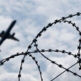 Ein Stacheldrahtzaun mit einem Flugzeug im Hintergrund.