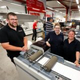 Ein Mann und zwei Frauen stehen um eine Druckmaschine.