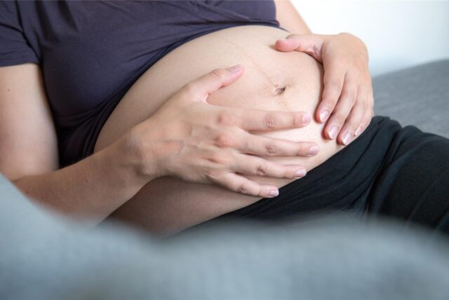 Schwangere Frau hält sich den Bauch.
