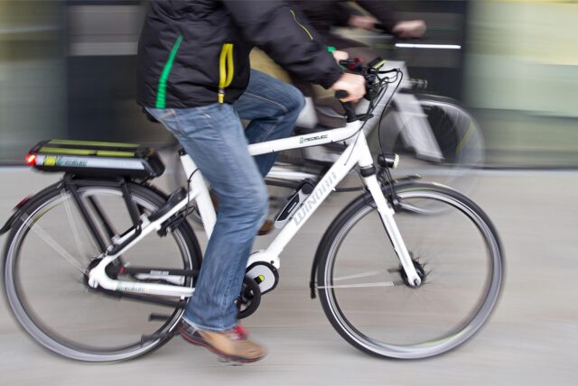 Eine Person sitzt auf einem weißen E-Bike und fährt zügig.