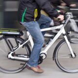 Eine Person sitzt auf einem weißen E-Bike und fährt zügig.