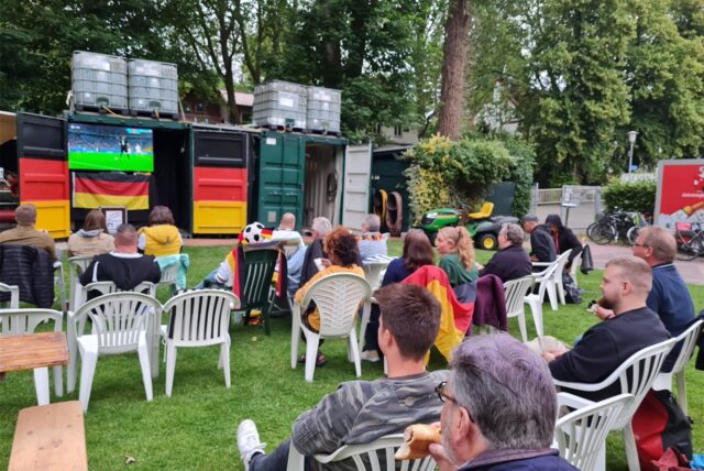 Im Freibad Bornekamp in Unna sitzen Zuschauer auf Stühlen auf der Wiese und schauen ein Fußballspiel an.