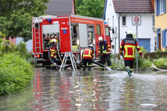Einsatzkräfte der Feuerwehr im Einsatz nach einem Unwetter mit Starkregen auf einer überfluteten Straße.