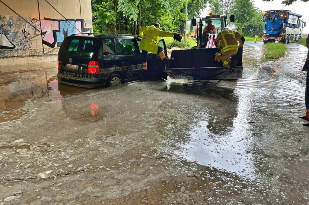 Auto steht in einer vollgelaufenen Unterführung. Feuerwehrmänner stehen drumherum. Auto steht in einer vollgelaufenen Unterführung. Feuerwehrmänner stehen drumherum.
