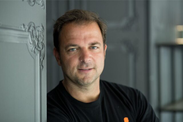 Hundeprofi Martin Rütter lehnt an einer Wand und schaut in die Kamera.