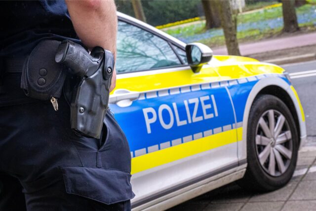 Polizist mit Waffe vor Polizeiauto