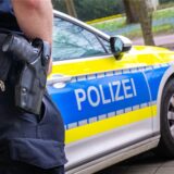 Polizist mit Waffe vor Polizeiauto