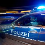 Ein Polizist sitzt in einem Streifenwagen, auf dem das Blaulicht eingeschaltet ist.