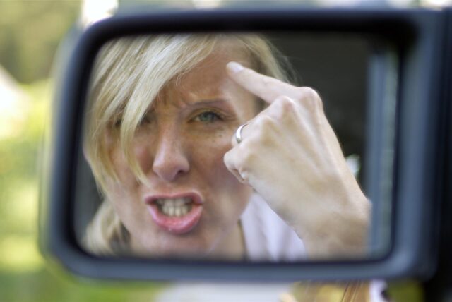 Eine Frau zeigt als Autofahrerin den Vogel.