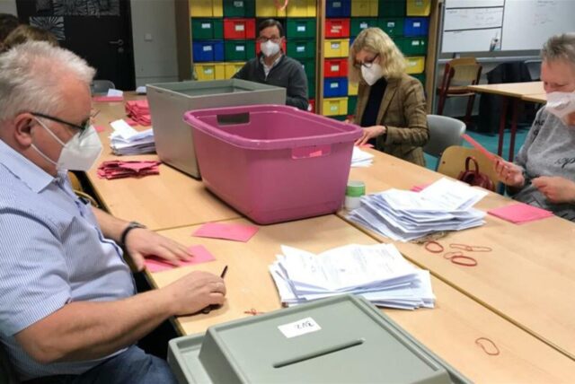 Menschen an einem Tisch mit Briefwahlunterlagen