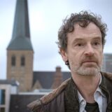 Tatort-Hauptkommissar Peter Faber (Jörg Hartmann) über den Dächern von Dortmund: Im Hintergrund ist die Petrikirche zu sehen.