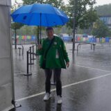 EM 2024-Volunteer Peter Planke steht mit einem blauen Regenschirm im strömenden Regen vor dem Dortmunder Stadion.