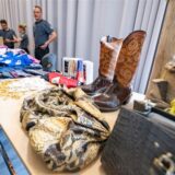 Auf einem Tisch stehen Cowboystiefel und Ledertaschen. Hinter dem Tisch stehen Mitarbeitende des Zolls, die die Ware kontrollieren.