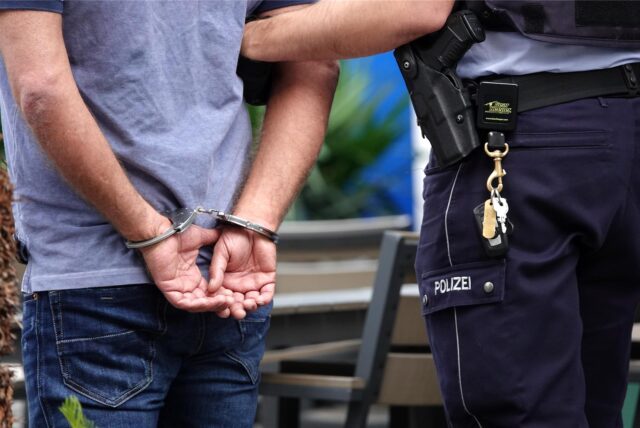 Ein Mann steht in Handschellen neben einem Polizisten (Symbolbild).