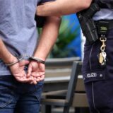 Ein Mann steht in Handschellen neben einem Polizisten (Symbolbild).
