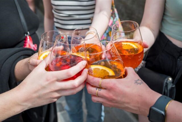 Mehrere Personen stoßen mit Gläsern, gefüllt mit Aperol Spritz, an.