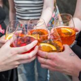 Mehrere Personen stoßen mit Gläsern, gefüllt mit Aperol Spritz, an.
