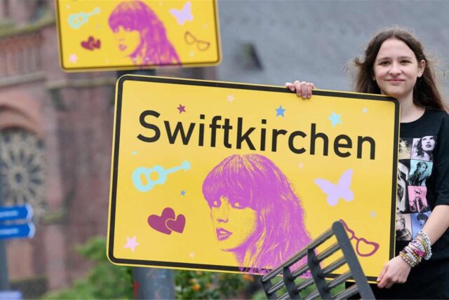 Ein Mädchen hält ein Ortsschild mit der Aufschrift „Swiftkirchen“.