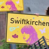 Ein Mädchen hält ein Ortsschild mit der Aufschrift „Swiftkirchen“.