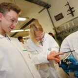 Einige Schüler stehen an einer Werkbank und arbeiten etwas an einem Schraubstock.