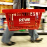 Eine Kundin mit einem tragbaren Plastikkorb mit REWE-Logo am Arm kauft ihre Lebensmittel in einem REWE-Supermarkt.