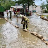 Ein Feuerwehrmann legt Sandsäcke auf eine überflutete Straße in Fröndenberg. Im Hintergrund stehen weitere Einsatzkräfte und Feuerwehrfahrzeuge