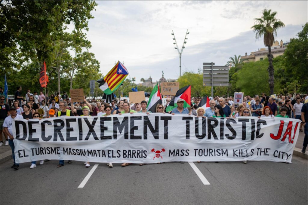 Spanier demonstrieren auf der Straße gegen den Tourismus. Sie halten einen großen weißen Banner vor sich.