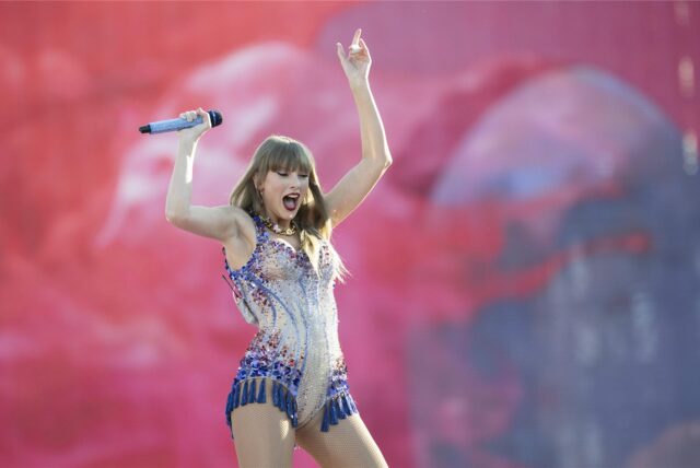 Die US-amerikanische Singer-Songwriterin Taylor Swift steht auf der Bühne und streckt ihre Arme in die Luft
