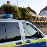 Im Vordergrund ist die Seite eines Polizeiwagens. Dieser steht am Seitenrand einer Straße an der ein Restaurant ist.