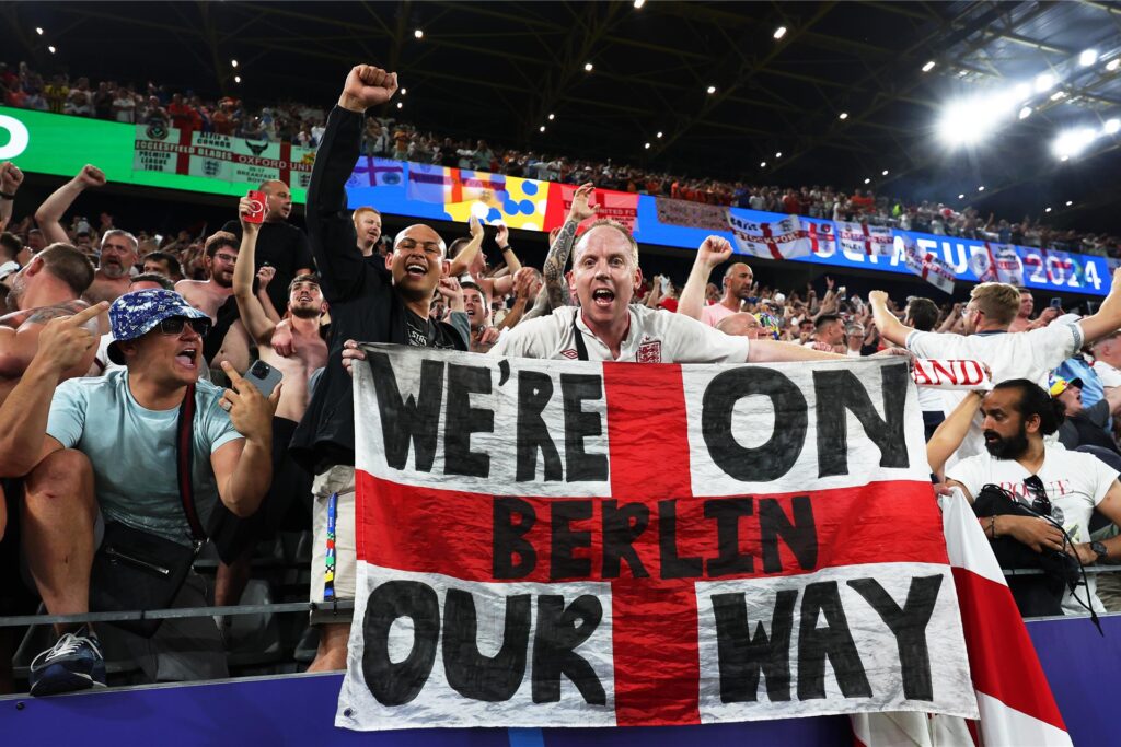 Englische Fans feiern den Einzug ihrer Nationalmannschaft ins Finale der Fußball-Europameisterschaft 2024. Die Flagge, die der Fan in die Kamera hält, trägt den Schriftzug Englische Fans feiern den Einzug ihrer Nationalmannschaft ins Finale der Fußball-Europameisterschaft 2024. Die Flagge, die der Fan in die Kamera hält, trägt den Schriftzug