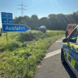Ein Auto steht auf der Wiese neben der A1-Ausfahrt in Schwerte. Am Straßenrand stehen die Polizei und ein Rettungswagen.