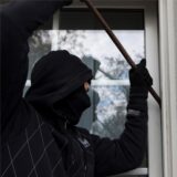 Ein Einbrecher bricht ein Fenster eines Wohnhauses auf.