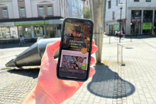 Eine Hand hält ein Smartphone in die Kamera, das die Internetseite von MyCityHunt zeigt.