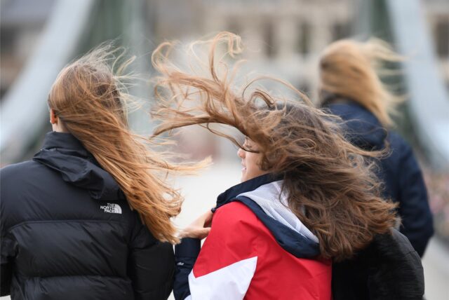Starker Wind wirbelt die Haare von zwei jungen Frauen auf.