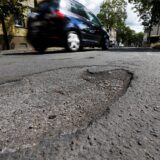 Ein großes Schlagloch im Hintergrund fährt ein Auto