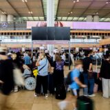 Zahlreiche Fluggäste warten am Hauptstadtflughafen BER vor einer schwarzen Anzeigetafel.