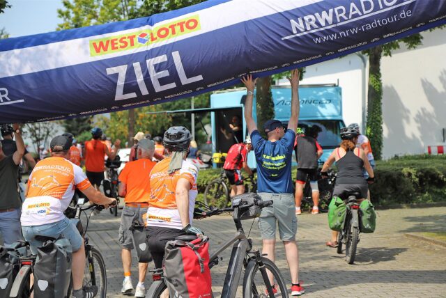 Mehrere Radfahrerinnen und Radfahrer überqueren die Ziellinie bei der NRW-Radtour 2024 in Fröndenberg am Samstag (20. Juli)
