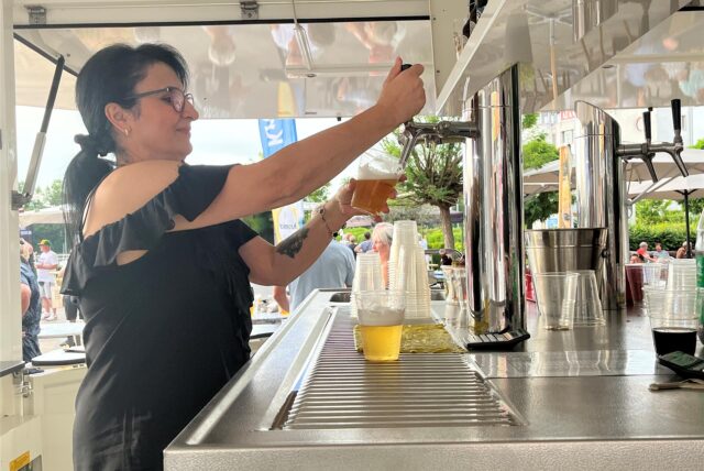 Eine Frau zapft an einem Bierstand ein Bier aus einem Zapfhahn.