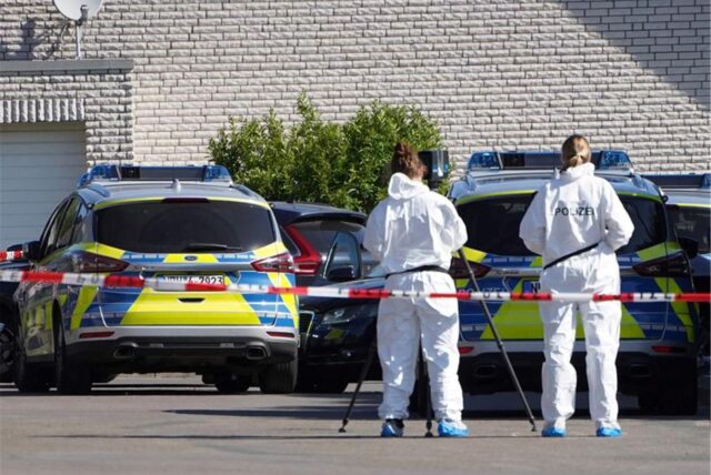 Beamte der Spurensicherung stehen hinter einer Absperrung der Polizei.